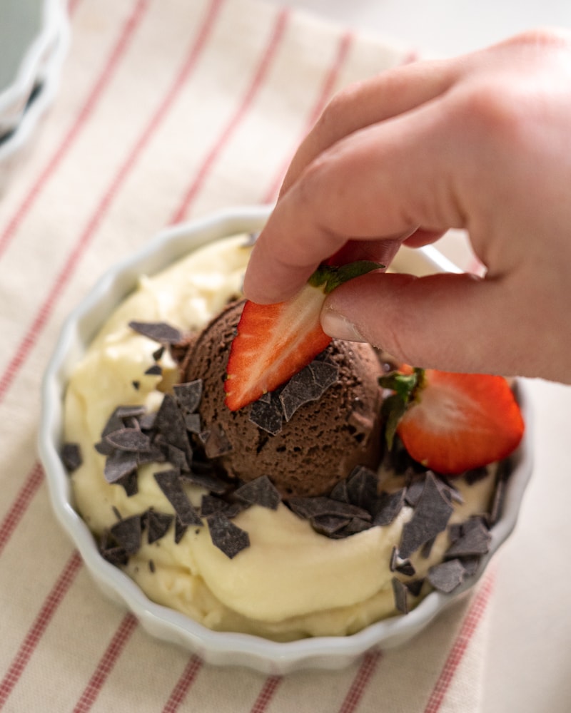 Auf diesem Bild siehst du wie Erdbeeren auf das Dessert gegeben werden.