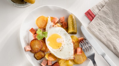 Das Bild zeigt in einer Pfanne angebratene Bratkartoffeln mit Leberkäse und zwei Spiegeleiern oben drauf. 