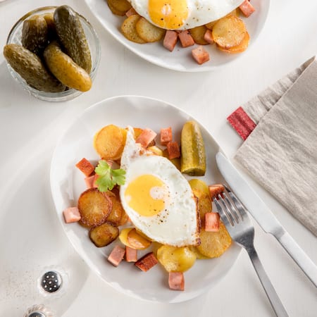 Das Bild zeigt in einer Pfanne angebratene Bratkartoffeln mit Leberkäse und zwei Spiegeleiern oben drauf. 