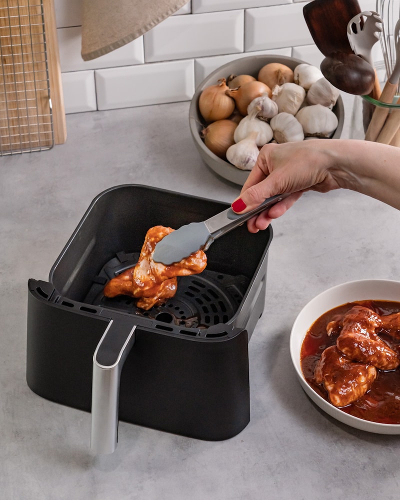 Dieses Bild zeigt, wie die Hähnchenflügel in die Heißluftfritteuse gelegt werden.