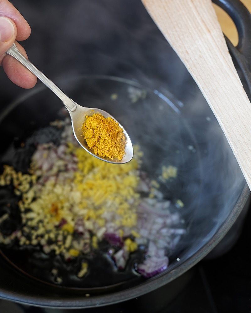 Dieses Bild zeigt, wie Currypulver hinzugegeben wird.