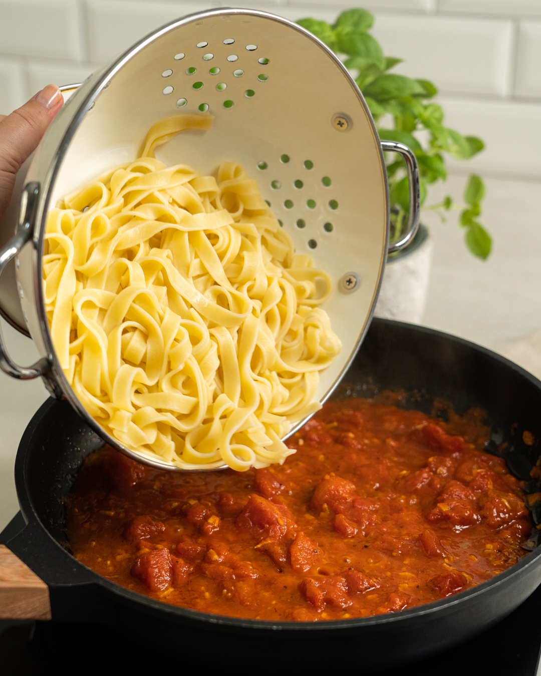 Auf diesem Bild siehst du wie die Tagliatelle in die Tomatensoße gegeben werden.