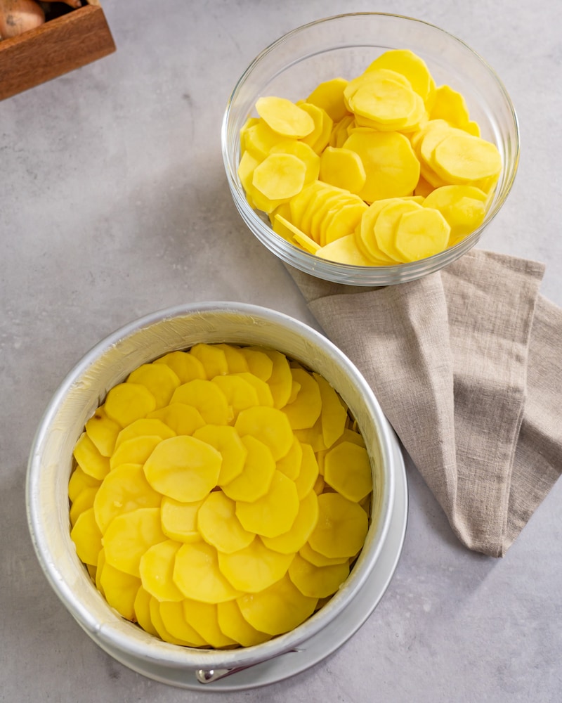 Dieses Bild zeigt wie eine Springform mit Kartoffelscheiben ausgelegt wird.