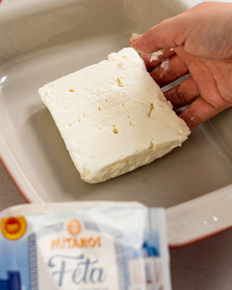 Auf diesem Bild siehst du wie ein Stück Feta in eine Auflaufform gegeben wird.