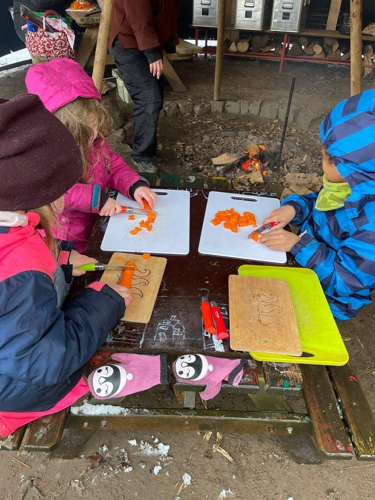 Kinder schneiden Karotten bei einer Feuerstelle