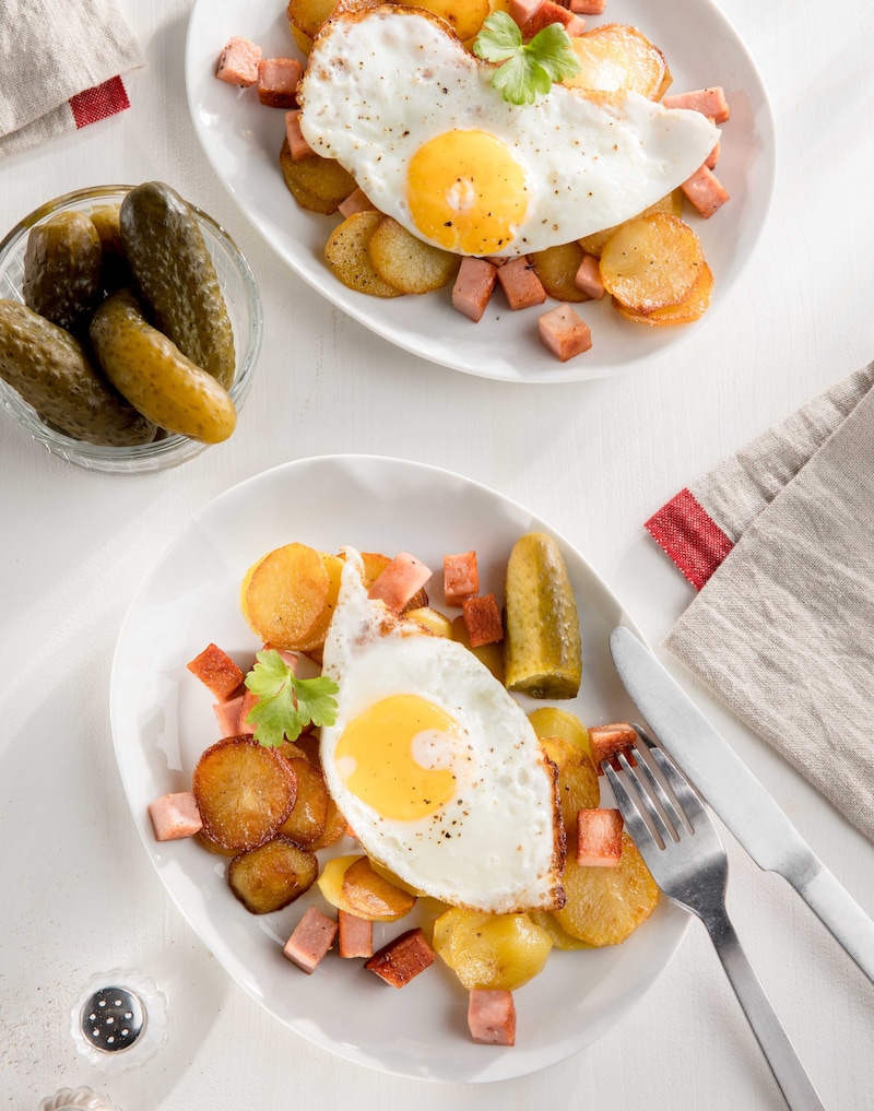 Das Bild zeigt in einer Pfanne angebratene Bratkartoffeln mit Leberkäse und zwei Spiegeleiern oben drauf. 