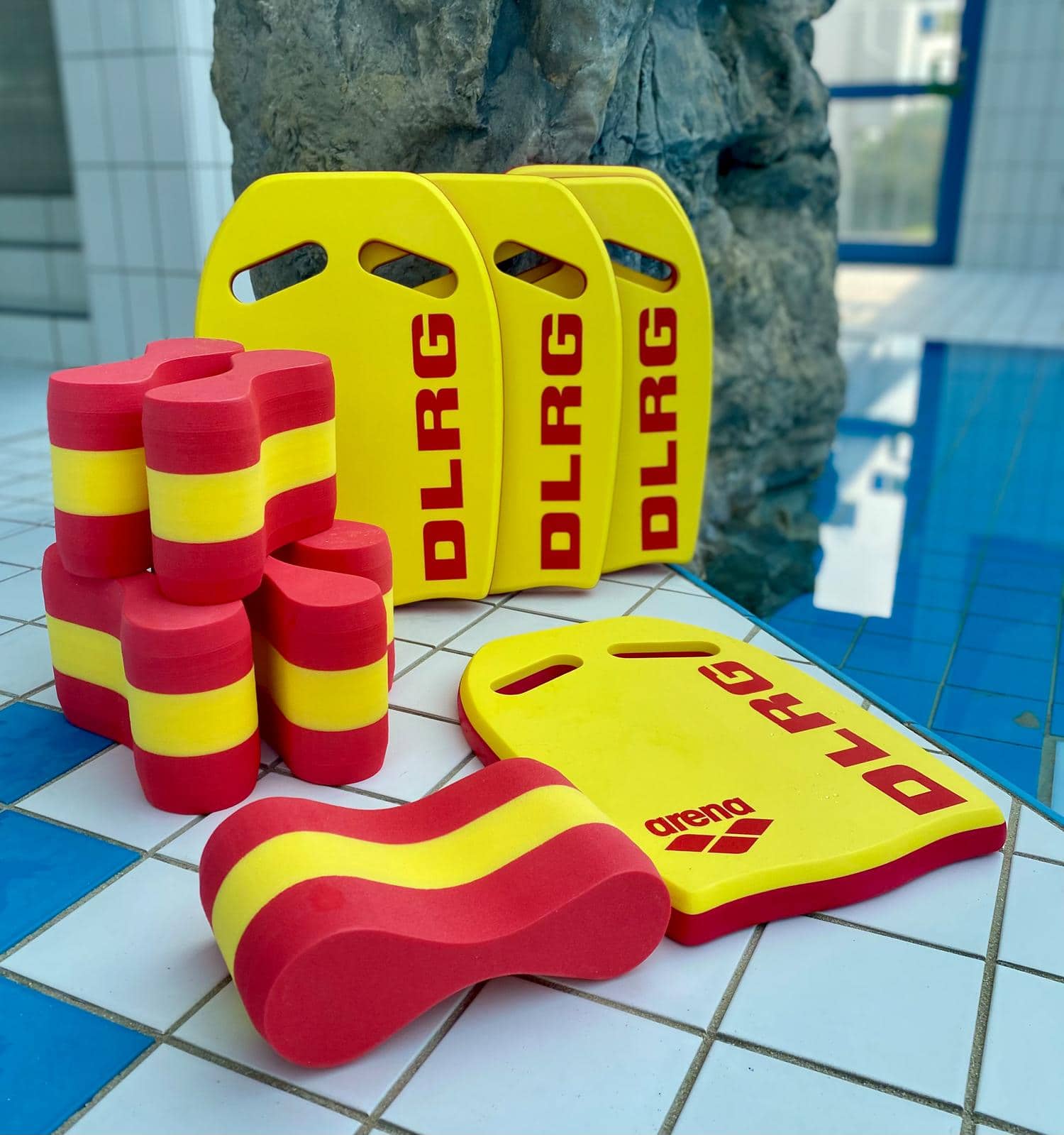 Verschiedene DLRG-Schwimmhilfen liegen neben einem Schwimmbecken