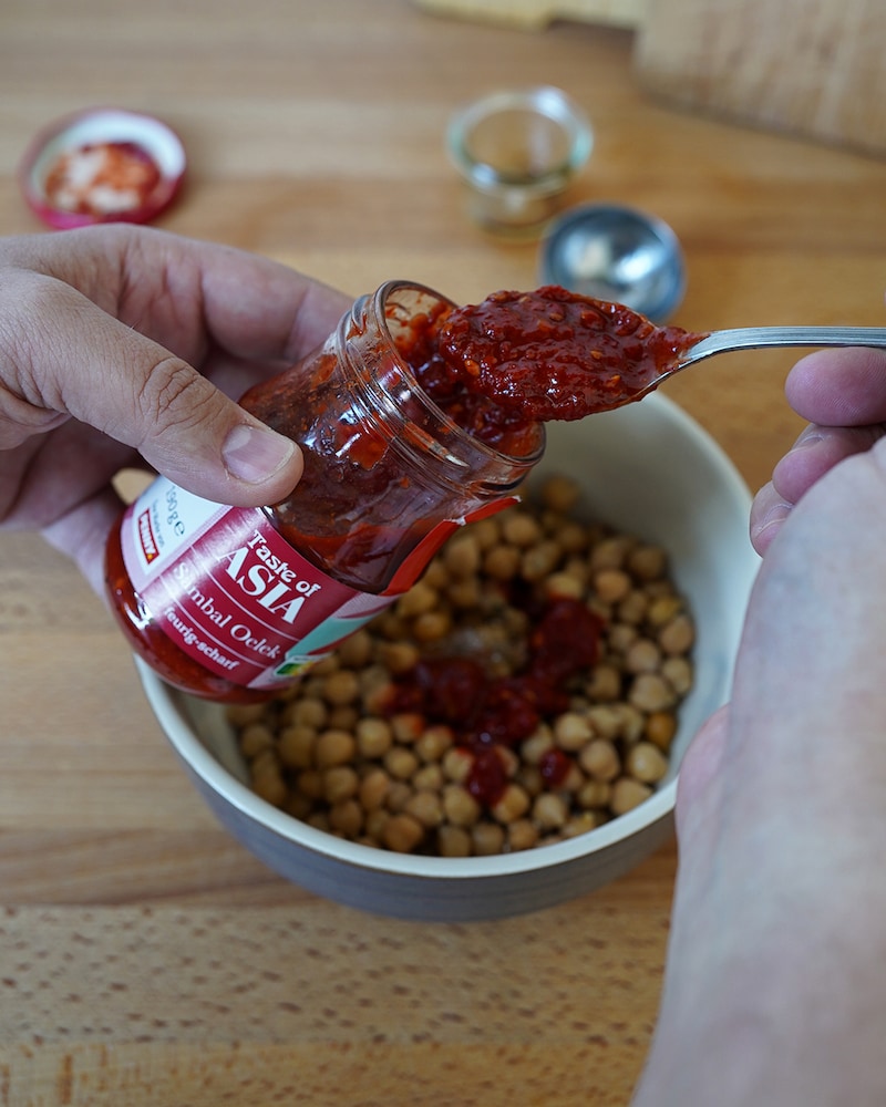 Dieses Bild zeigt das Würzen der Kichererbsen mit Sambal Oelek.