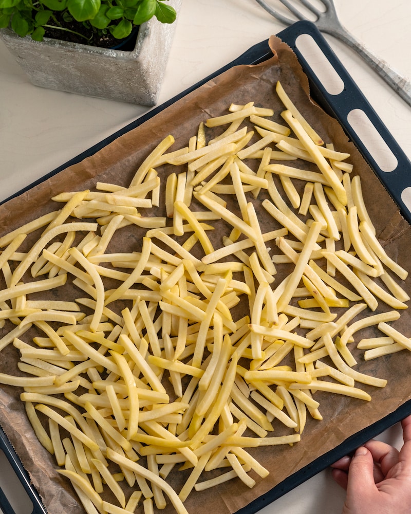 Auf diesem Bild siehst du wie Pommes auf ein Backblech gegeben werden.