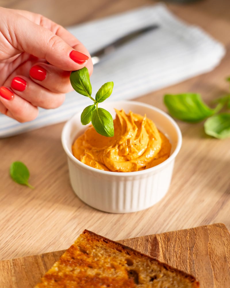 Dieses Bild zeigt wie die Blättchen Basilikum auf die Tomatenbutter gegeben werden.