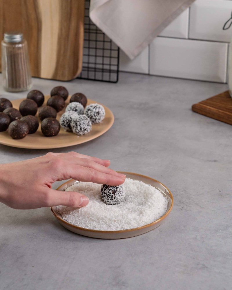 Dieses Bild zeigt wie die Bällchen in Kokosraspeln gewälzt werden.