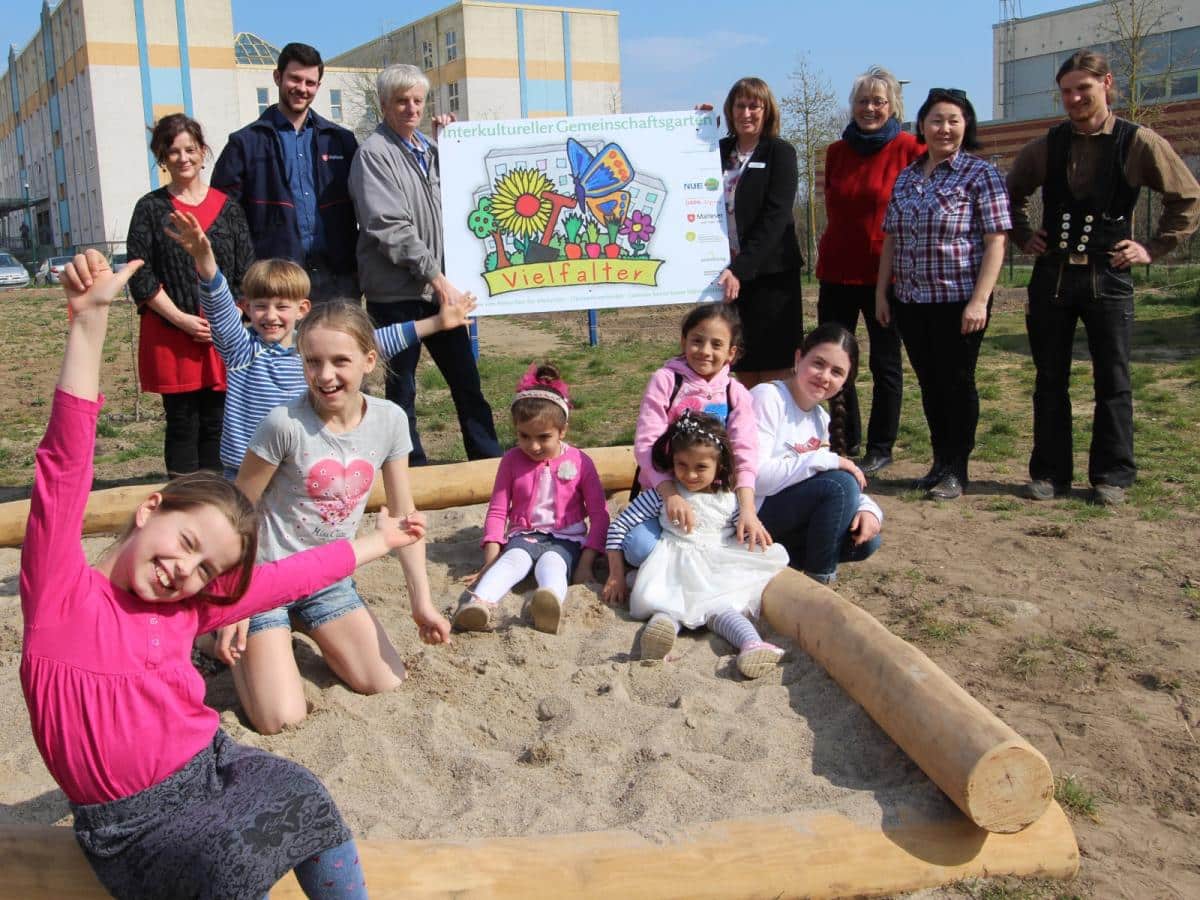 Vereinsmitglieder und Kinder im Sandkasten laecheln froehlich in die Kamera