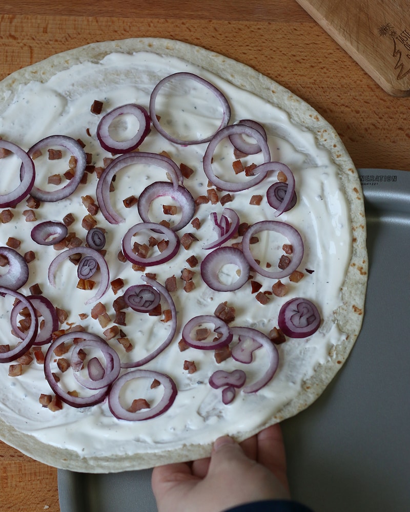 Auf diesem Bild siehst du wie der herzhafte Flammkuchen aufs Blech gelegt wird.