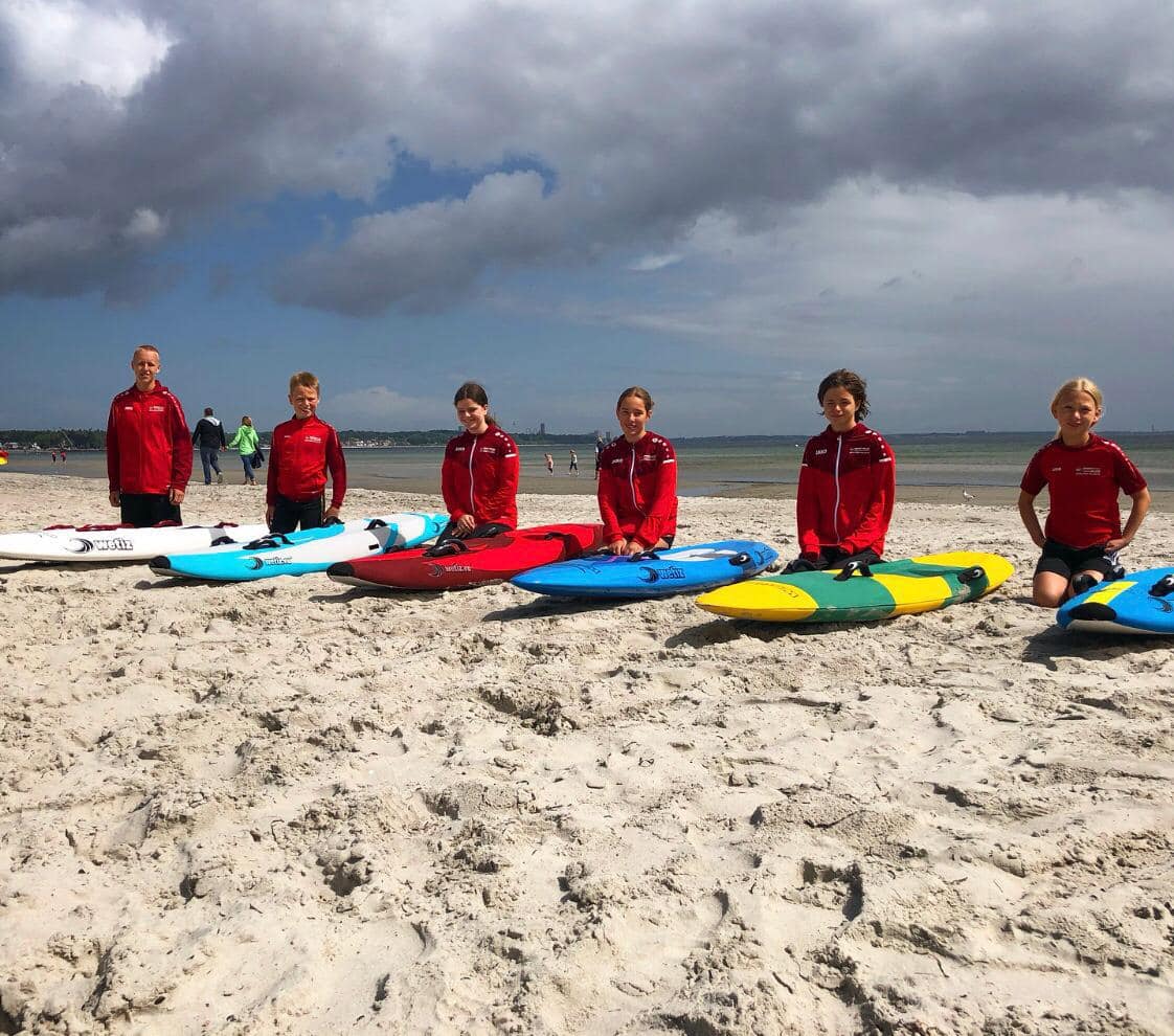 Kinder sitzen laechelnd mit ihren Kayaks am Strand