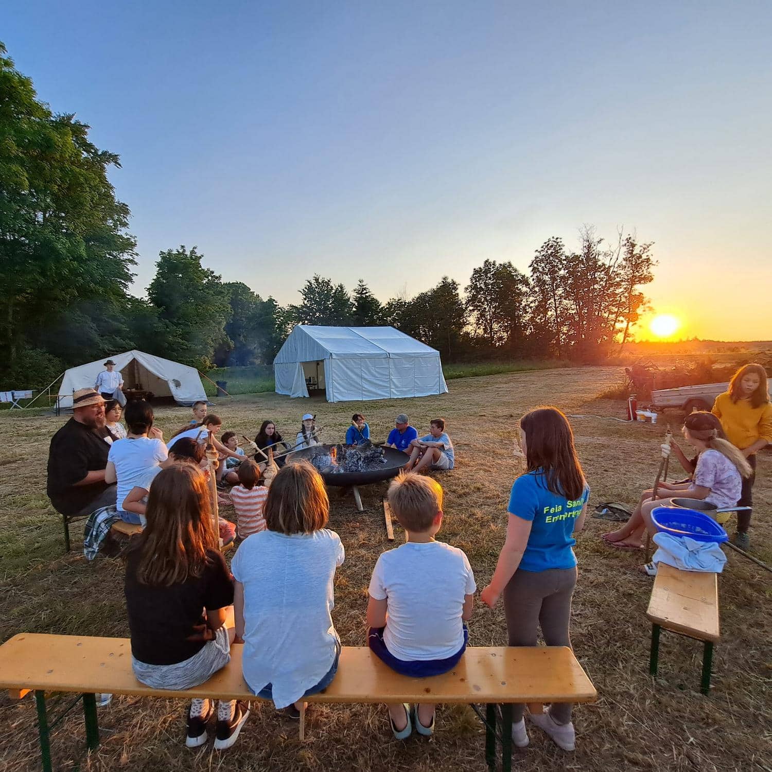 Kinder und Vereinsmitglieder backen Stockbrot am Lagerfeuer bei Sonnenuntergang
