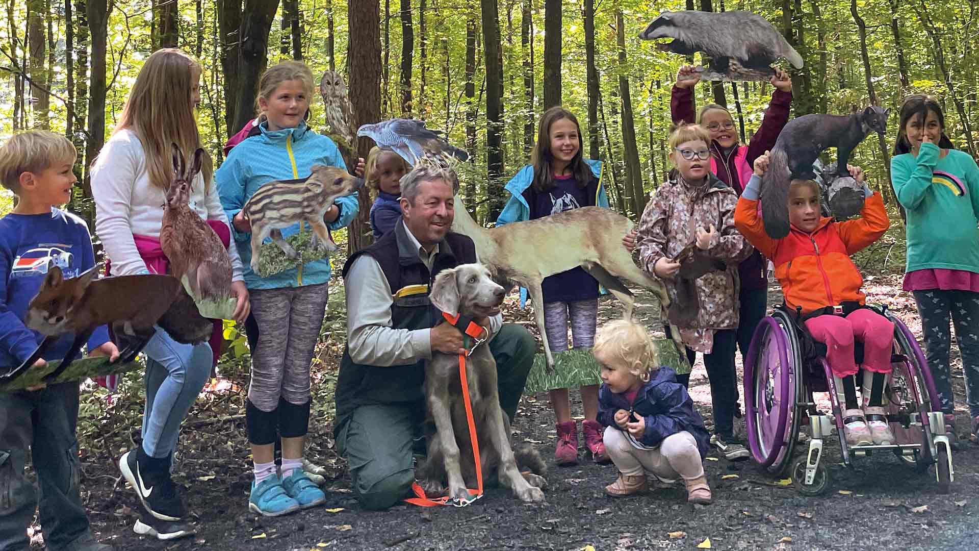 Kindergruppe steht im Wald mit Papierfiguren