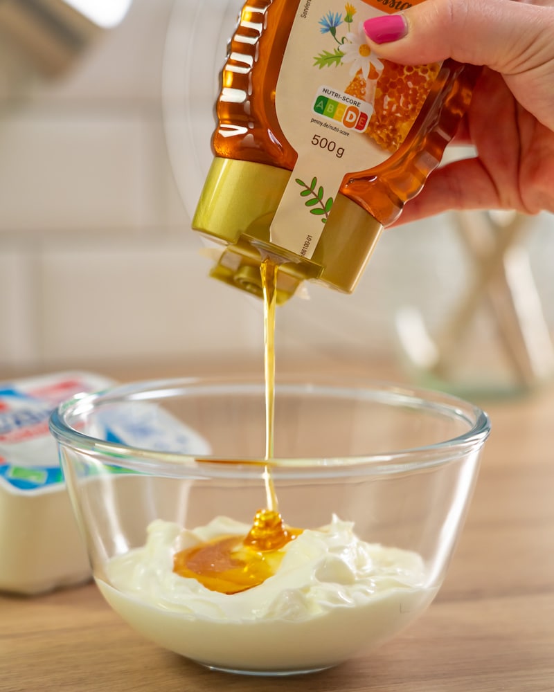 Dieses Bild zeigt, wie der Quark mit Honig gesüßt wird. 