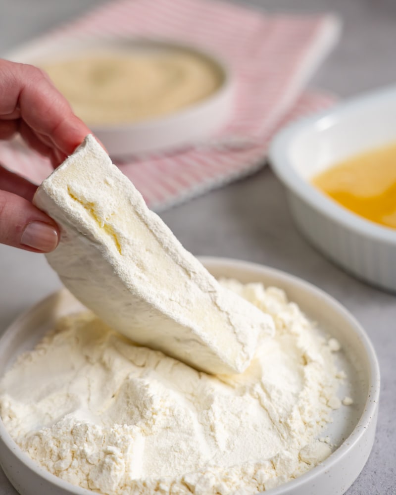 Dieses Bild zeigt wie der Camembert in Mehl gegeben wird.