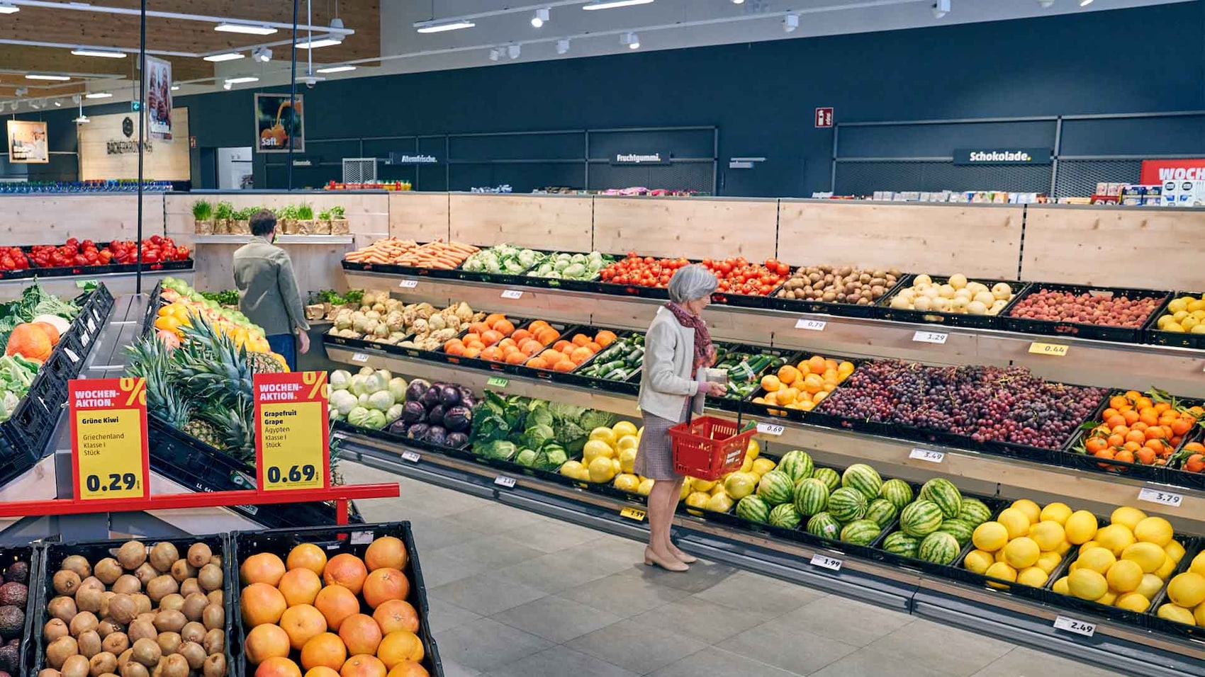 Eine Kundin mit Einkaufskorb schaut sich in der Obst- und Gemüseabteilung um.