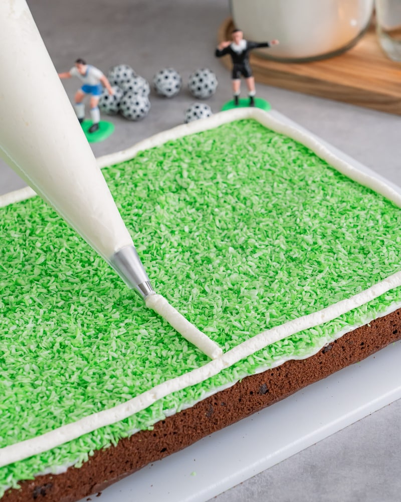 Diese Bild zeigt wie der fertige Fussballkuchen vom Blech dekoriert wird.