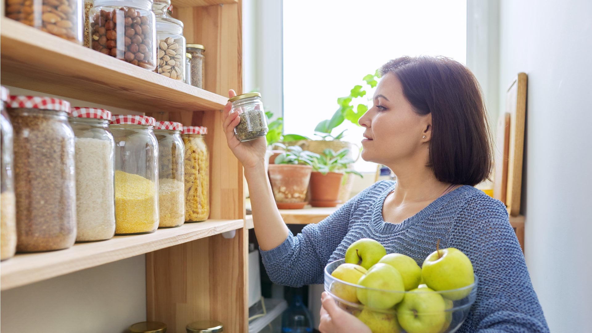 Braunhaarige Frau steht vor einem Regal mit Lebensmitteln in Glasbehältern und schaut sich ein kleines genauer an. 
