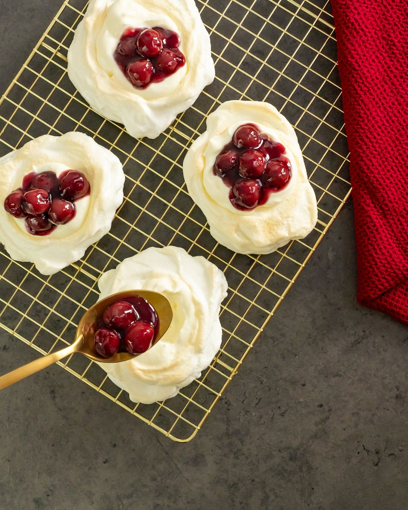 Dieses Bild zeigt wie die Kirschen in die Pavlovas gegeben werden.