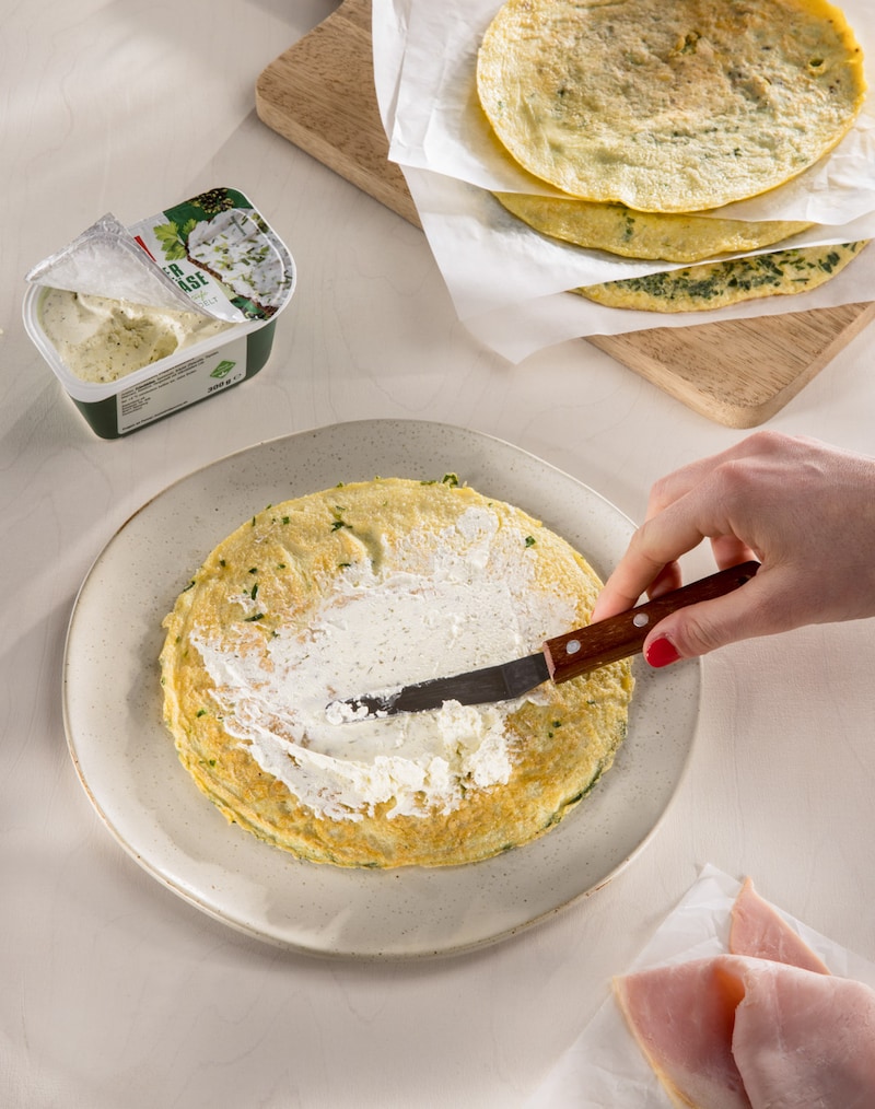 Dieses Bild zeigt wie ein Omelett mit Frischkäse bestrichen wird.