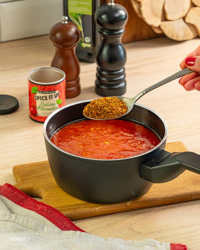 Dieses Bild zeigt wie die Gewürze zur Tomatensoße dazugegeben werden.