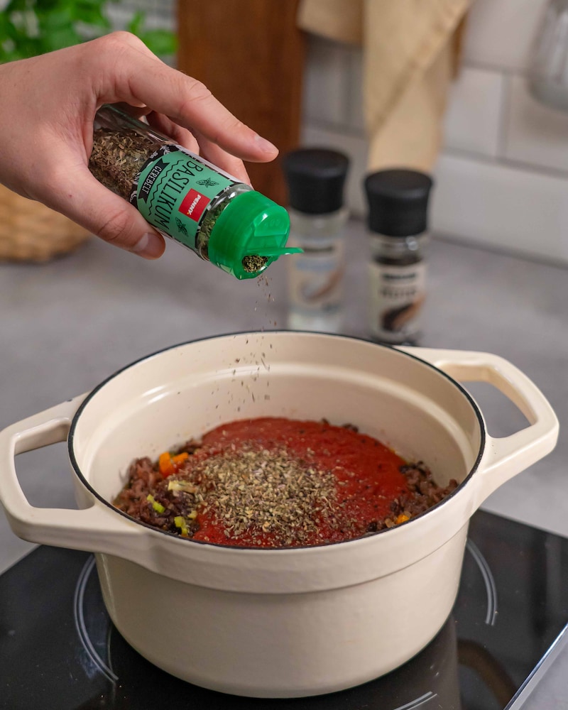 Dieses Bild zeigt, wie der Basilikum in die Tomatensauce gegeben wird.