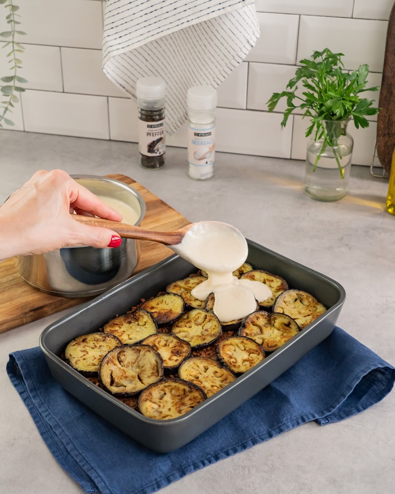 Auf diesem Bild siehst du wie die Bechamelsoße auf das Hackfleisch gegeben wird.