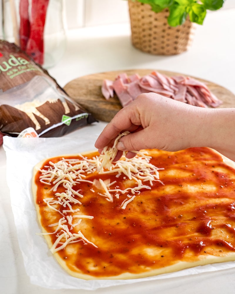 Das Bild zeigt wie die Pizza mit Käse bestrichen wird.