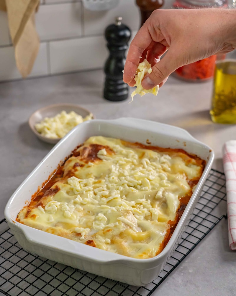 Dieses Bild zeigt, wie die Lasagne mit Käse bestreut wird.