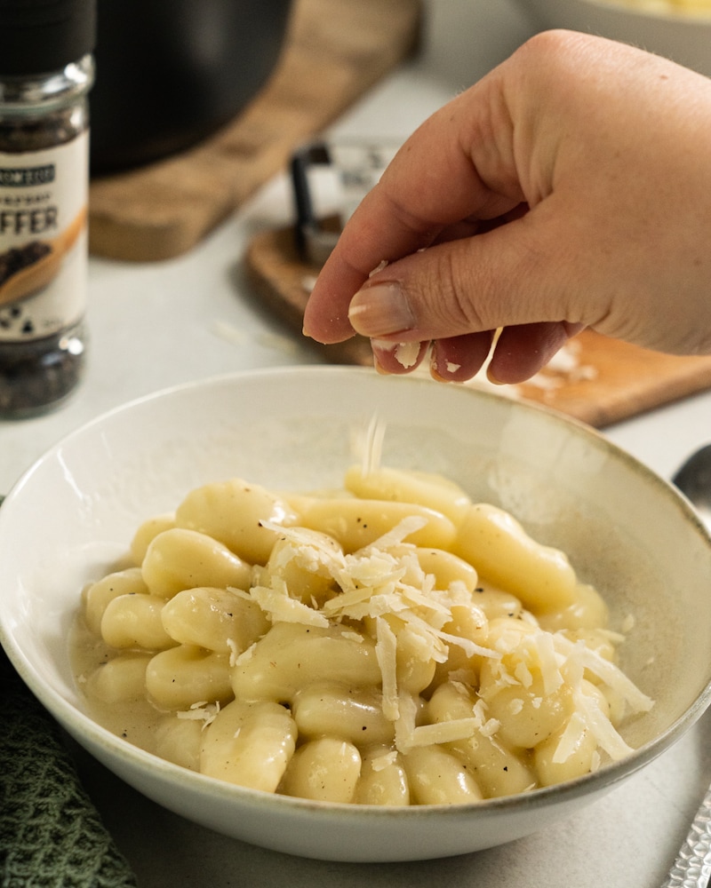 Auf diesem Bild siehst du wie die fertigen Gnocchi mit Käse bestreut werden.