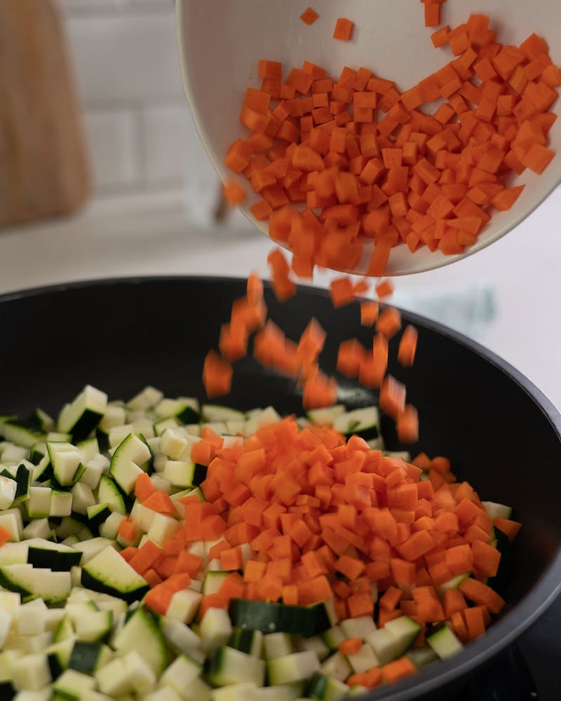 Dieses Bild zeigt wie Zucchini und Möhren in die Pfanne gegeben werden.