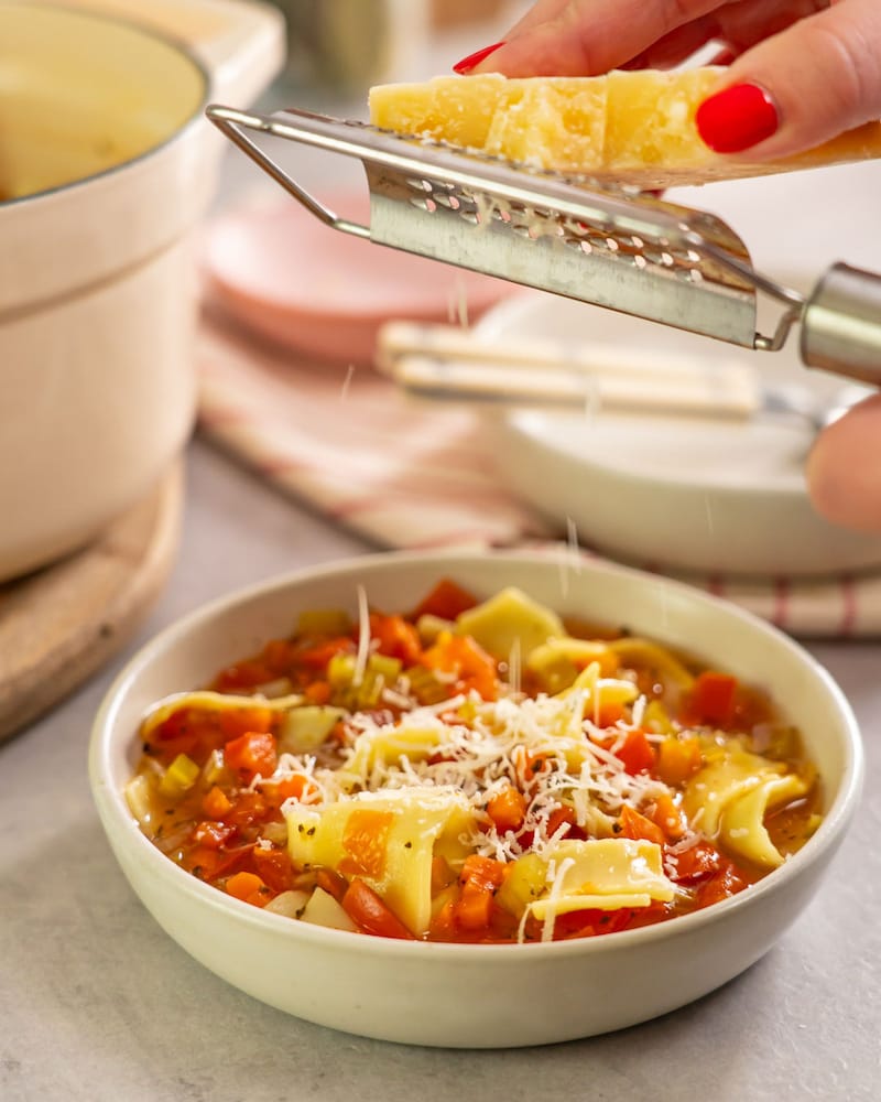 Dieses Bild zeigt wie der Grana Padano über die Lasagnesuppe gerieben wird.