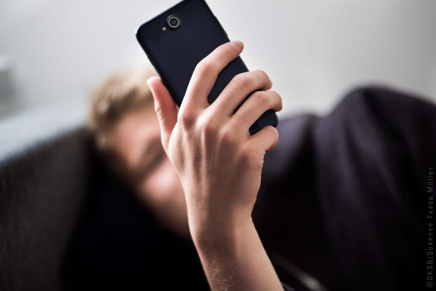 Eine verschwommene Person schaut auf ihr Handy im Vordergrund