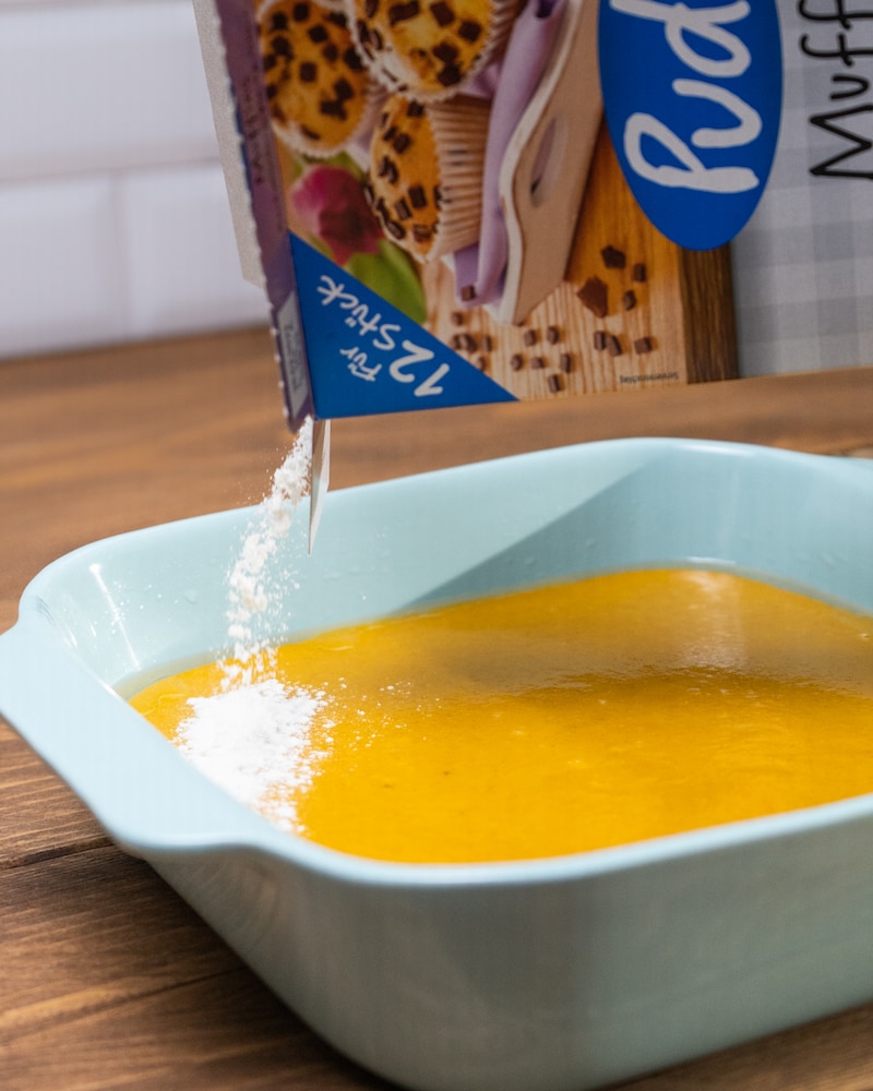 Auf diesem Bild siehst du wie auf die Kürbiscreme eine Muffinbackmischung gegeben wird.