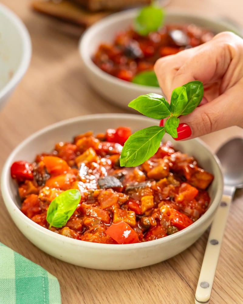Dieses Bild zeigt wie die Caponata mit Basilikum dekoriert wird.