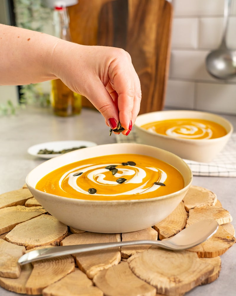 Dieses Bild zeigt wie die Suppe mit Kürbiskerne verziert wird.