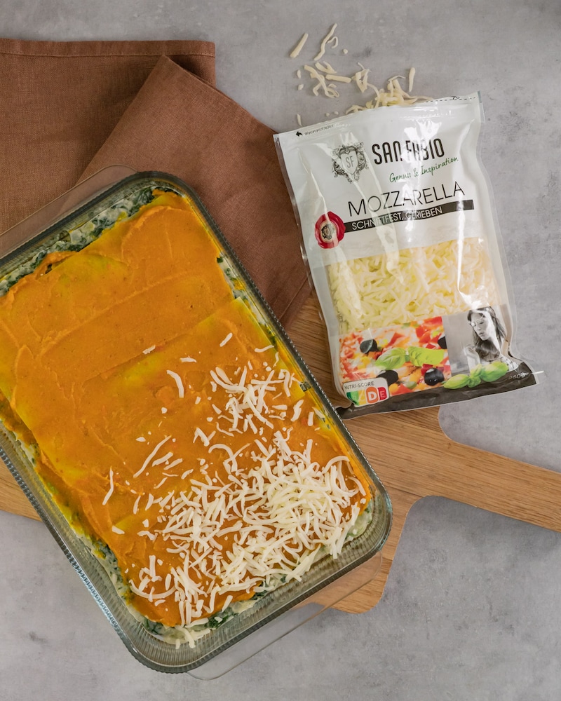 Dieses Bild zeigt wie die Lasagne mit Käse bestreut wird.