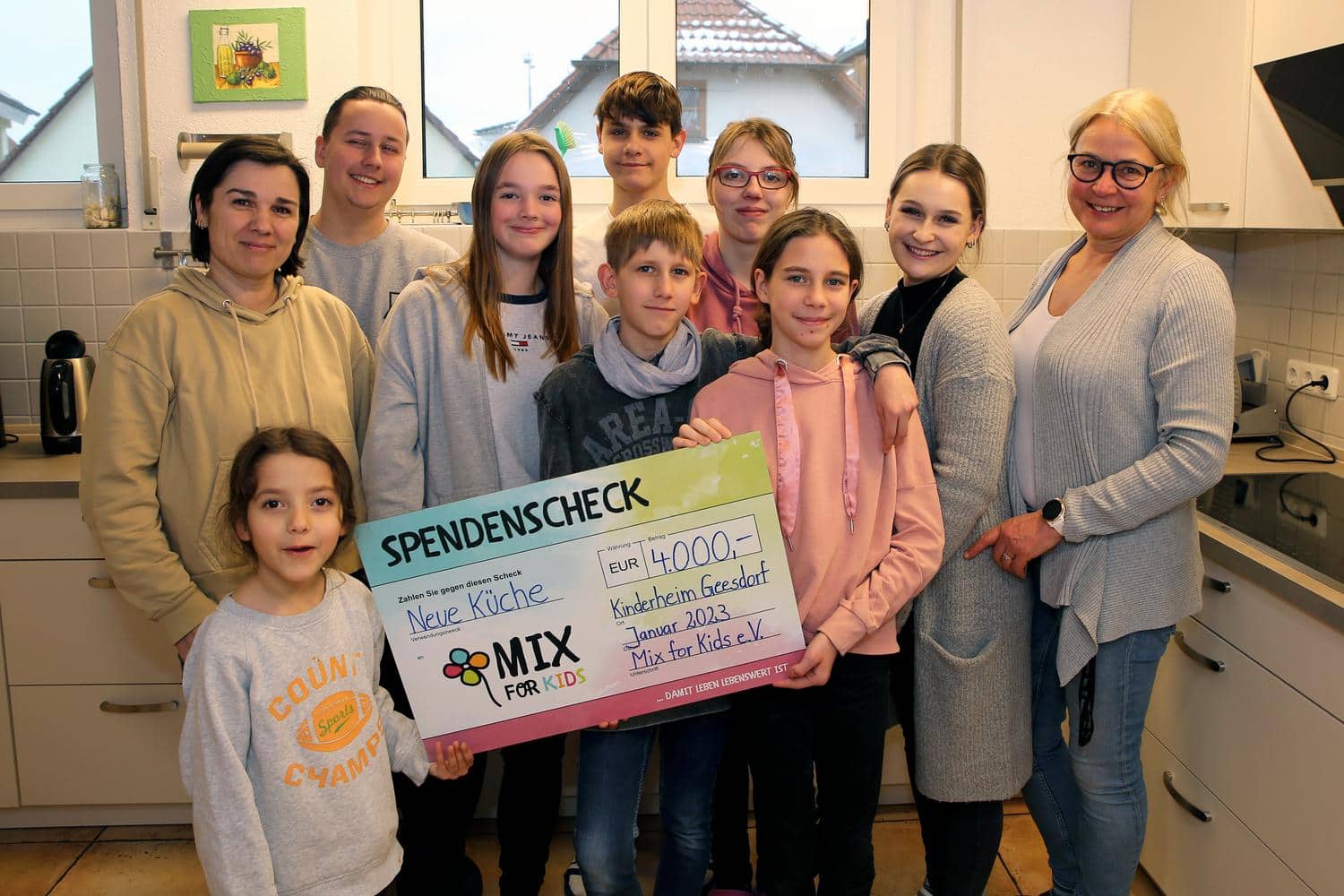 Kinder und Vereinsmitglieder halten froehlich einen Spendenscheck in die Kamera