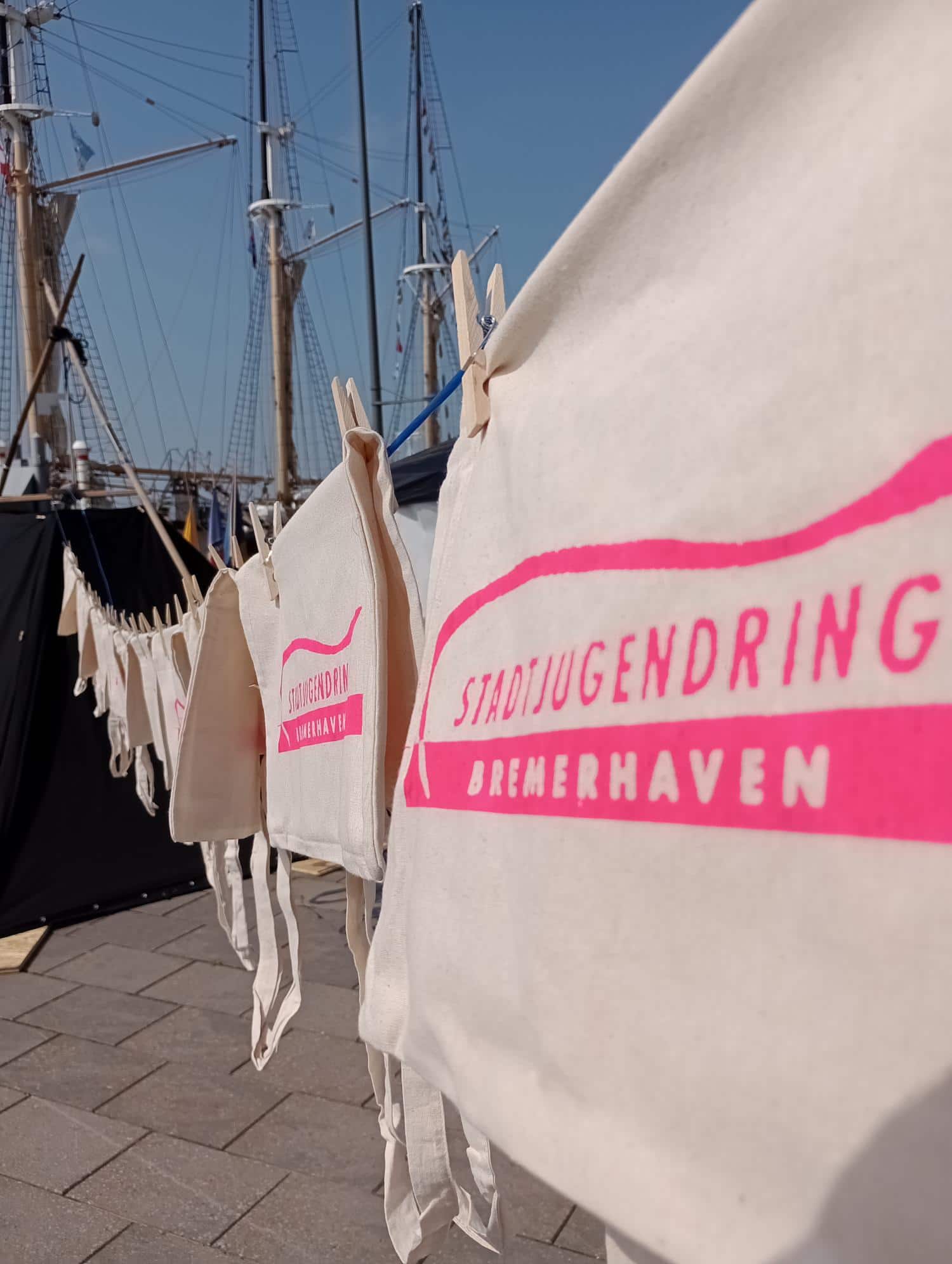 Mit dem Vereinslogo bedruckte Jutebeutel haengen auf einer Waescheleine am Hafen