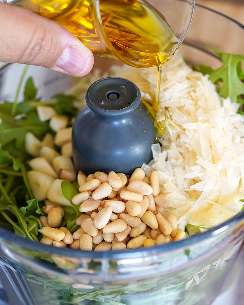 Dieses Bild zeigt wie Ruccola, Pinienkerne, Parmesan und Öl in einen Mixer gegeben werden.