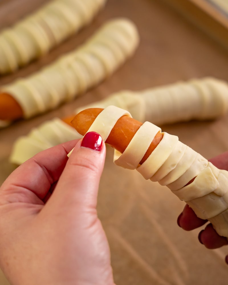 Dieses Bild zeigt wie die Würstchen in den Teig eingewickelt werden.