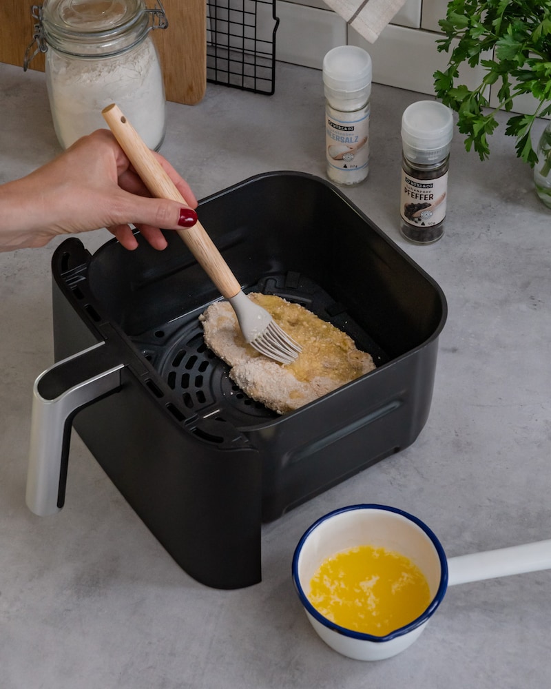 Diese Bild zeigt wie das Schnitzel im Airfryer mit Fett bestrichen wird.
