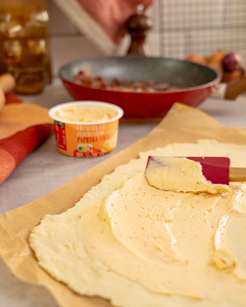 Dieses Bild zeigt wie der Teig mit dem Frischkäse bestrichen wird.