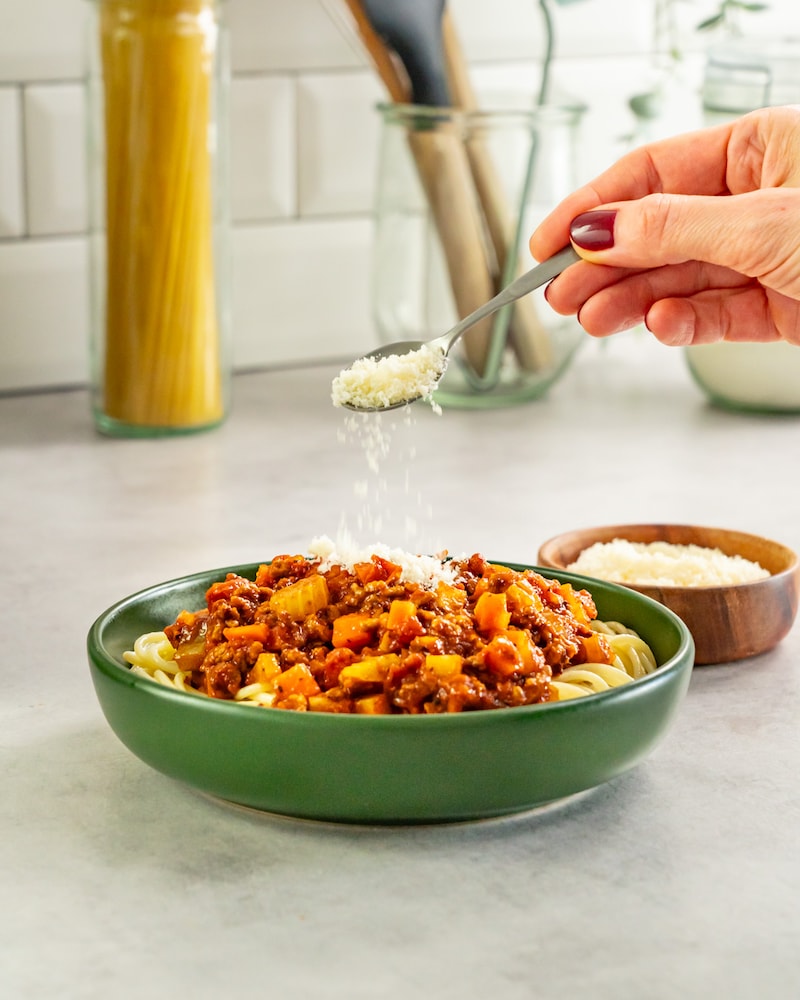 Dieses Bild zeigt wie der Käse über die Spaghetti Bolognese gegeben wird.