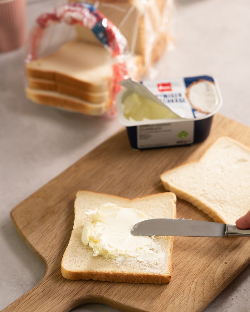 Dieses Bild zeigt wie Frischkäse auf eine Toast-Scheibe geschmiert wird.