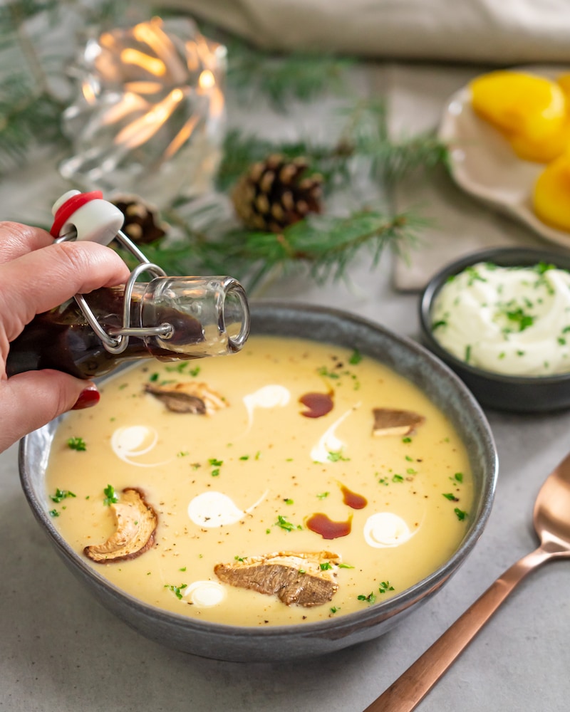 Dieses Bild zeigt wie die Suppe auf einem Teller angerichtet wird und mit Kürbiskernöl verfeinert wird.