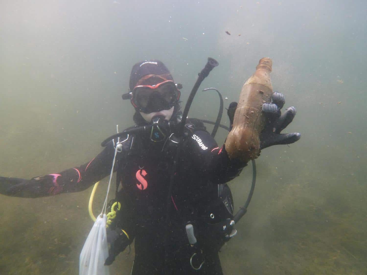 Ein unter Wasser tauchendes Vereinsmitglied haelt eine alte Plastikflasche in die Kamera